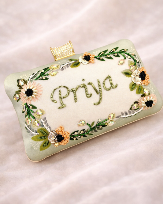 Clutch bag with floral design and 'Priya' embroidery on a light background