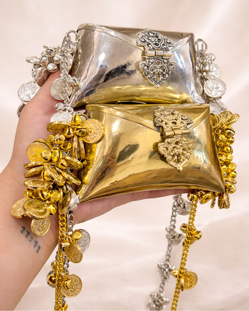 Gold and silver handbag with decorative elements held by a hand against a neutral background