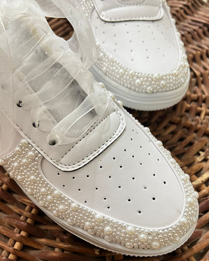 White sneakers with pearl embellishments on a woven surface