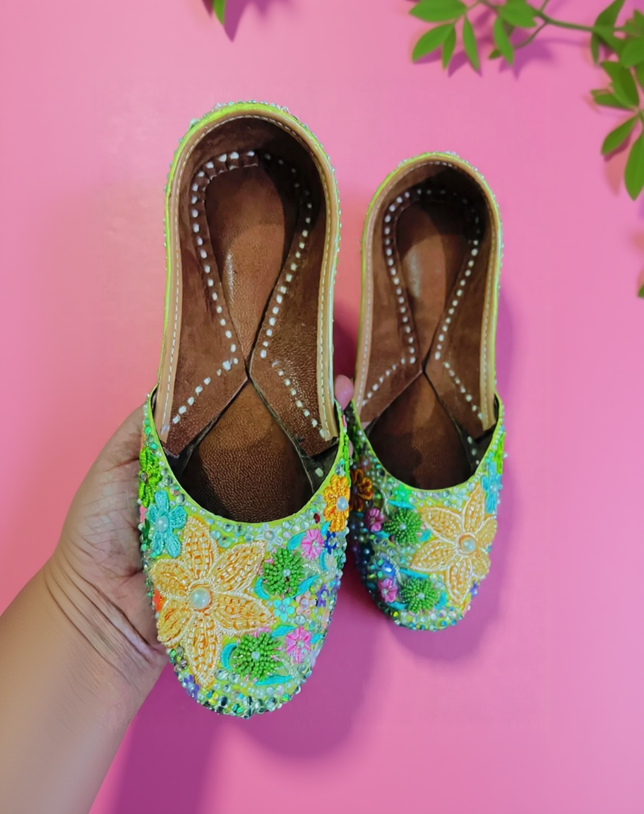 Colorful embroidered shoes held against a pink background